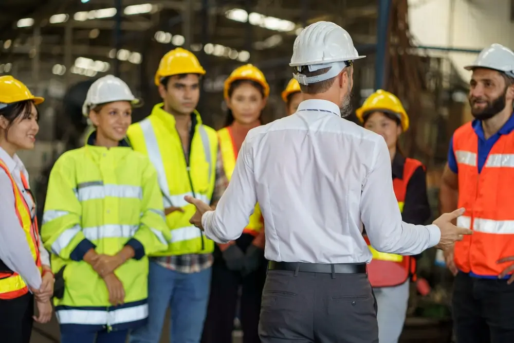 Group of diversity engineer factory worker standing in morning meeting with business man manager or executive boss leader team talking and brief in industry manufacturing warehous.e