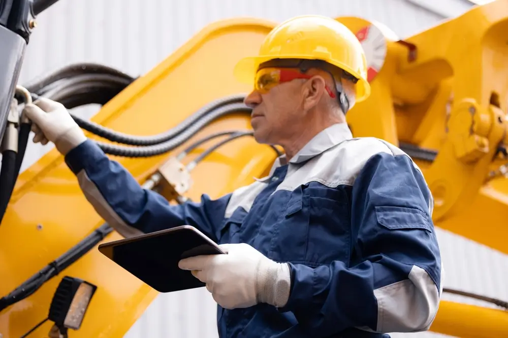 Machinery tractor mechanic with tablet computer checks hydraulic piston hose system equipment on excavator.