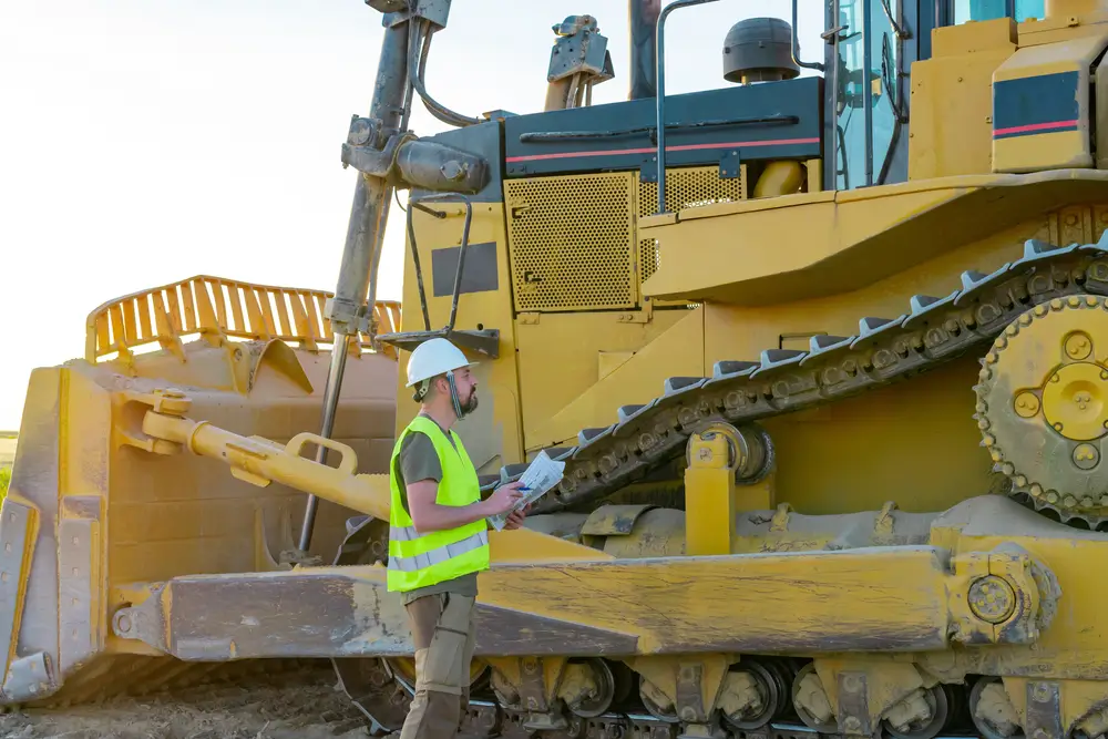 Hipster construction manager with a beard and safety helmet inspects a work machine. heavy machinery, excavator