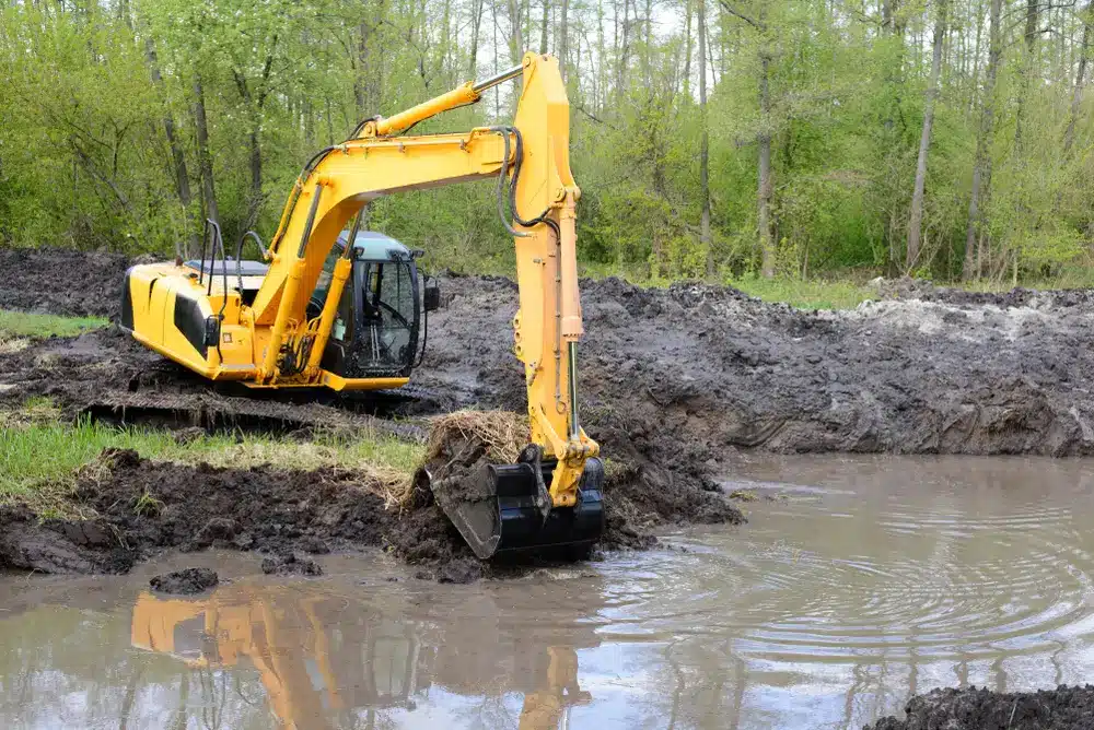 Big powerful excavator digging drainage channel in swamp in countryside.