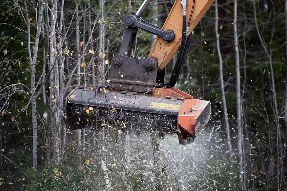 Mulching head on boom of an excavator clearing vegetation from side of road.