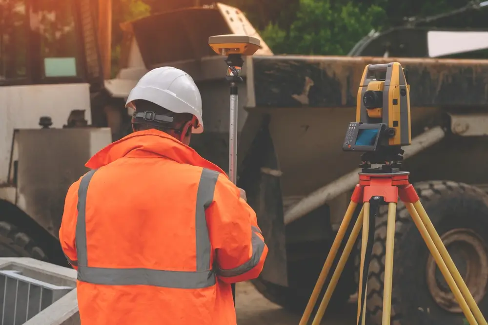 Surveyor site engineer with total positioning station on the construction site of the new road construction with construction machinery and materials  in the background.