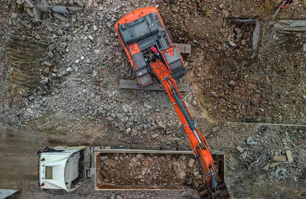 Top-down view of an excavator loading debris into a large truck at the demolition site in Gdansk, Poland, showcasing the efficiency of the industrial machinery in rubble clearance.